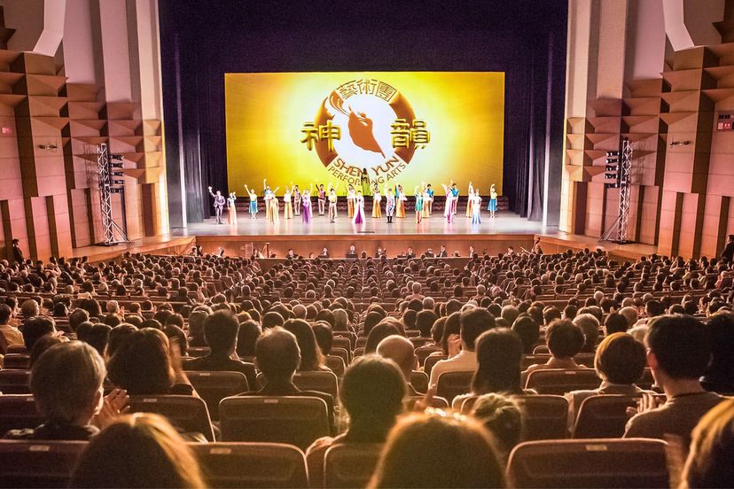 満員の客席。神韻のロゴが映る舞台に出演者が並んでいる
